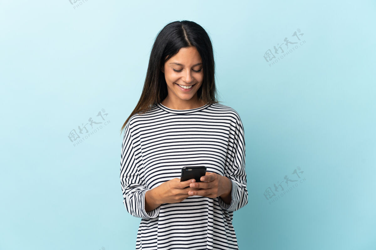 手机被隔离在蓝色墙上的白人女孩用手机发信息移动电话通信