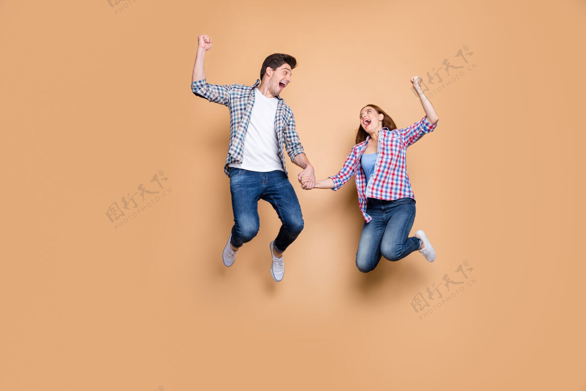 运动全尺寸照片两人疯狂女士家伙跳高庆祝最佳胜利举起拳头销售购物牵手穿休闲格子牛仔裤衣服孤立米色背景惊人头发运动