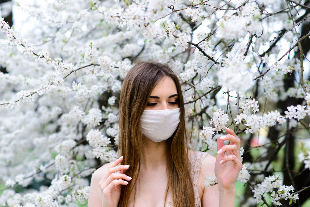 花园在春天的花园里 一个戴着无菌医用防护口罩的年轻女子空气流行病冠状病毒