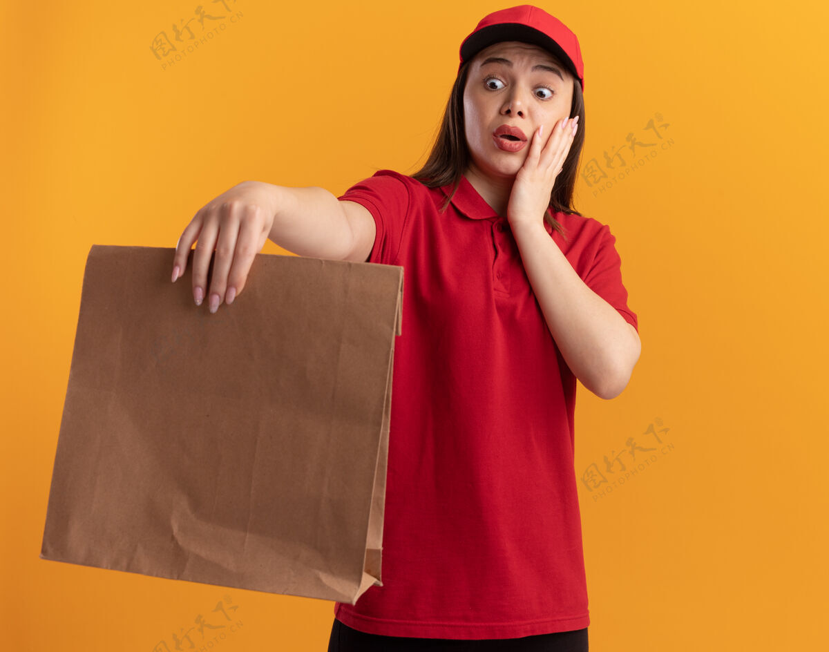 橘子焦急漂亮的女送货员穿着制服把手放在脸上拿着 看着纸包送货纸女人
