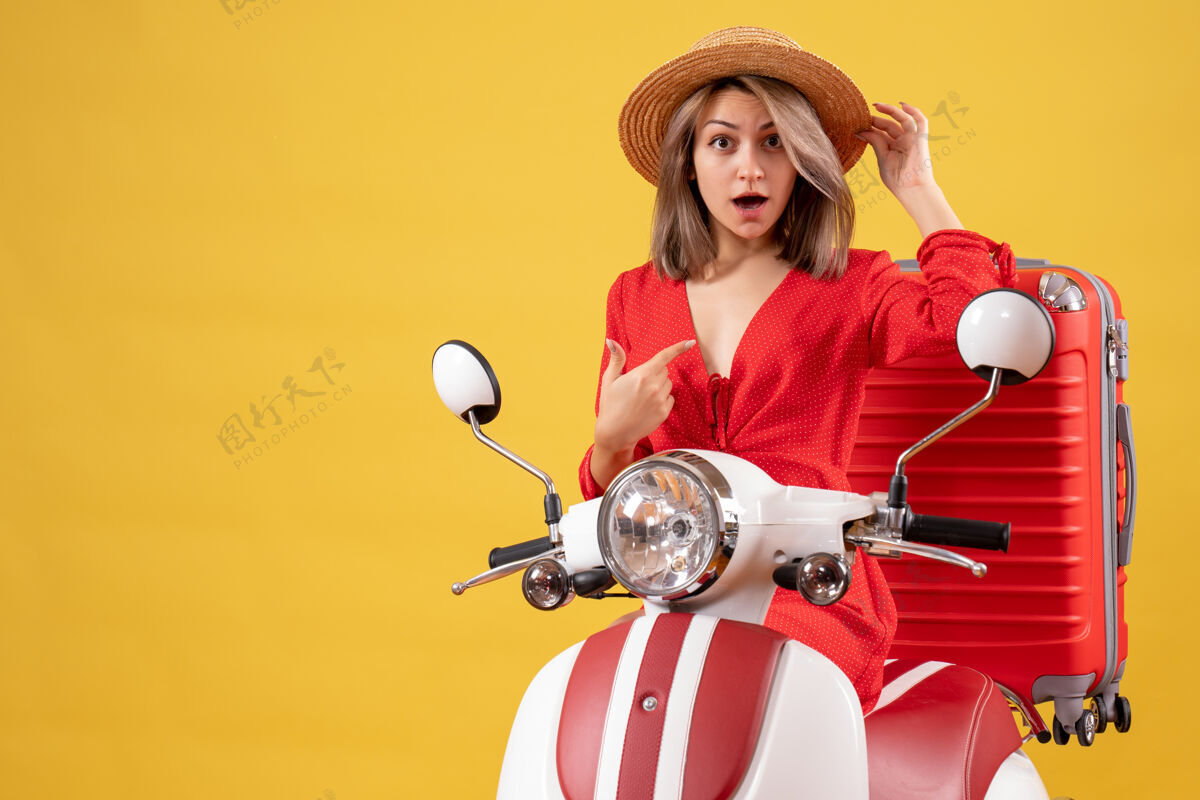 时尚骑着轻便摩托车的漂亮女孩 红色手提箱指着自己漂亮女孩肖像模特