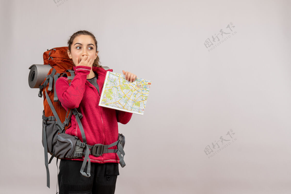 背包年轻的旅行者背着背包 在灰色的地图上举着地图 心里很纳闷可爱成人肖像