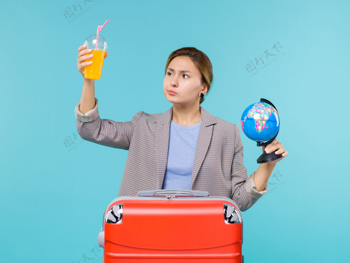 观点正面图：度假中的女性手持新鲜果汁和地球仪在蓝色背景下进行海上旅行度假微笑人女人