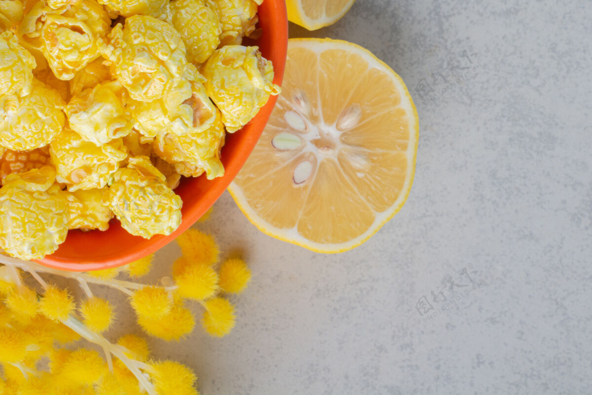 鲜花一碗涂着焦糖的爆米花 柠檬片和一束蓬松的花放在大理石表面蓬松爆米花外套