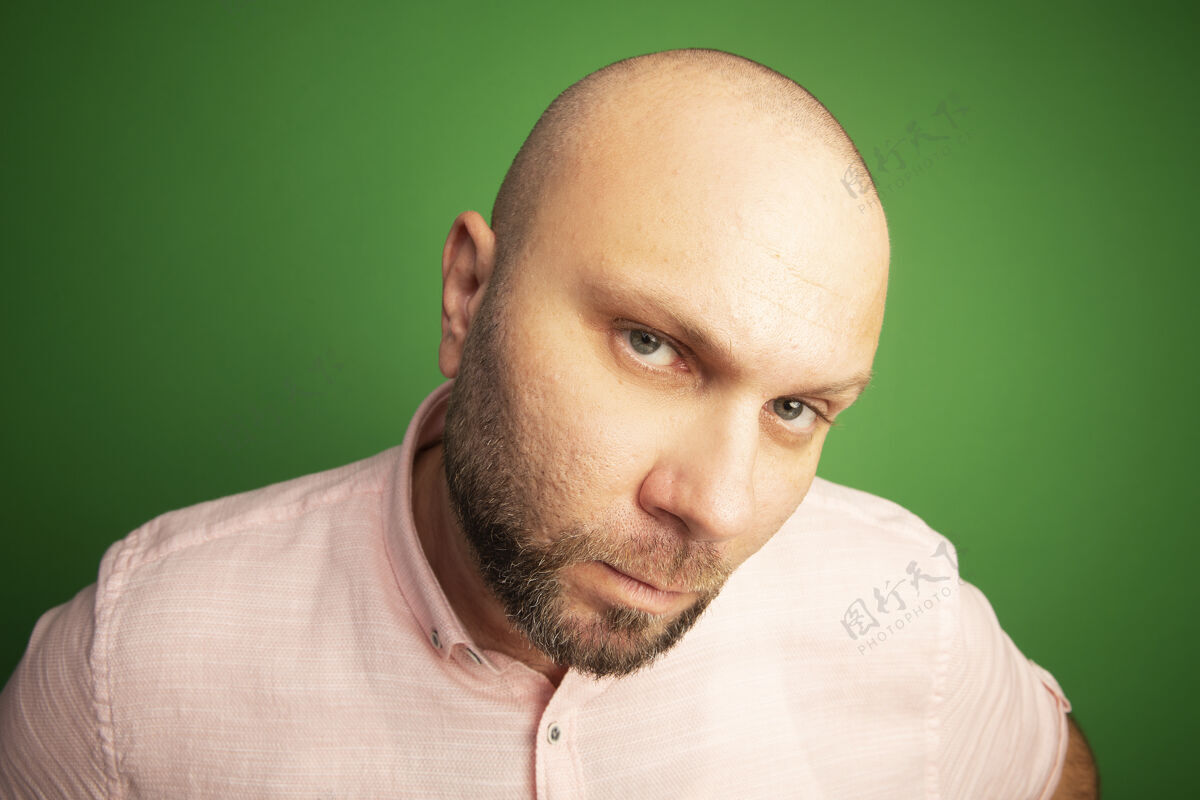 绿色一个穿着粉色t恤的中年秃头男人 目光直勾勾地站在绿色的一边秃头严格穿
