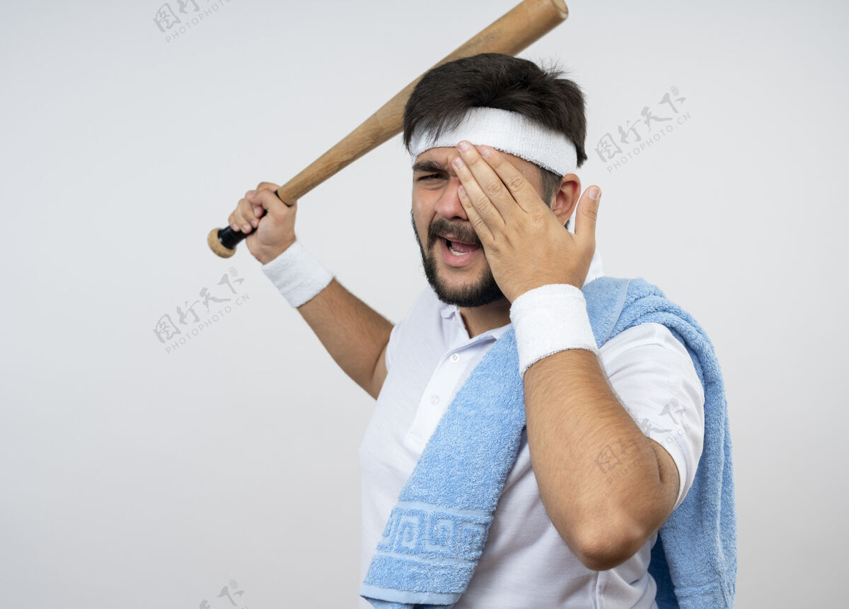 年轻未被释放的年轻运动男子戴头带和手环与毛巾在肩上提出棒球棒覆盖的脸与手隔离在白色墙壁与复制空间头带男人穿