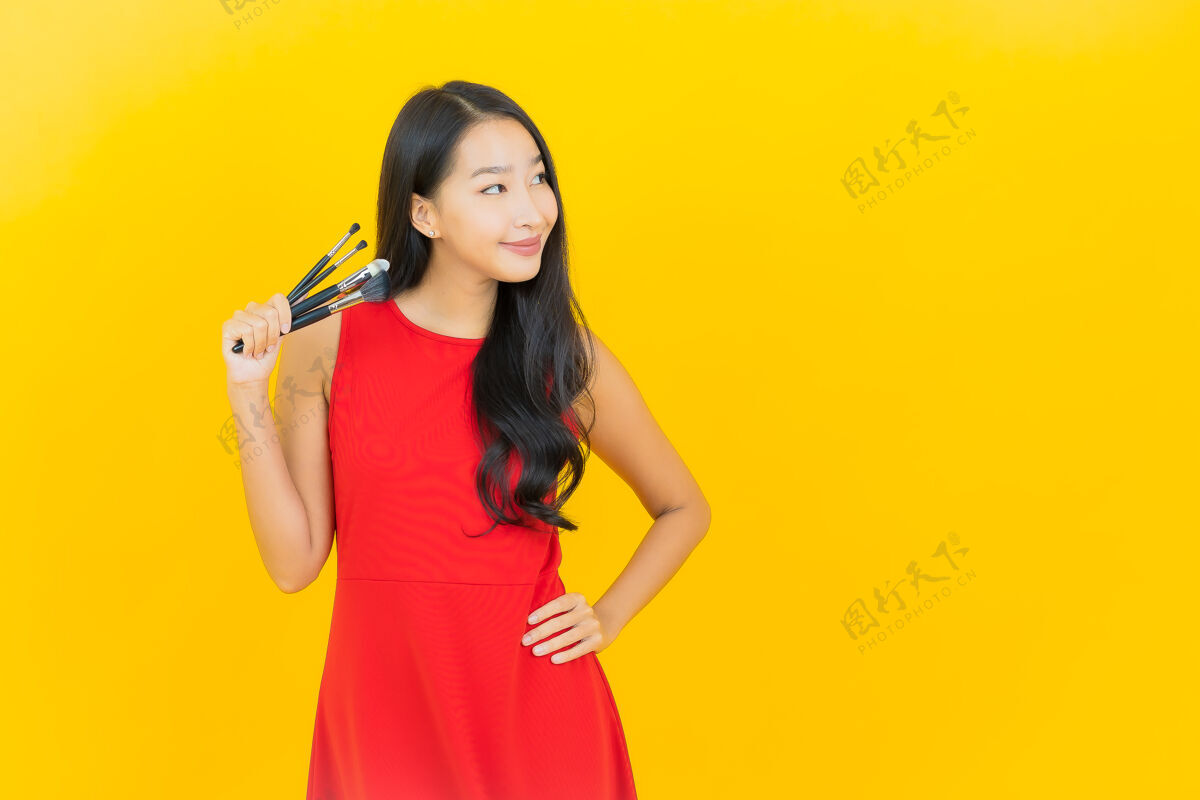魅力用化妆刷在黄色墙上描绘美丽的亚洲年轻女子魅力黑发画笔