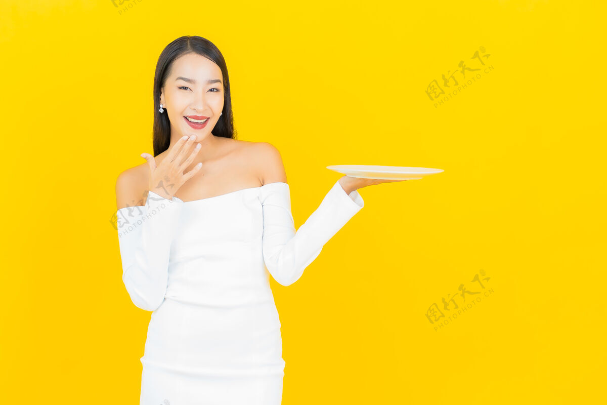 甜点美丽的亚洲商界年轻女子的画像 黄色墙上有空盘子快乐成人员工