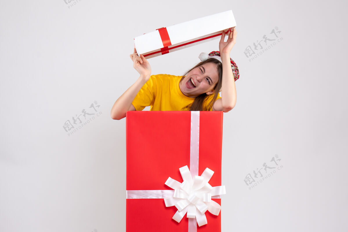 抱前视图可爱的女孩与圣诞老人帽子升起盒盖在她的头后站在大圣诞礼物盒子圣诞老人帽子