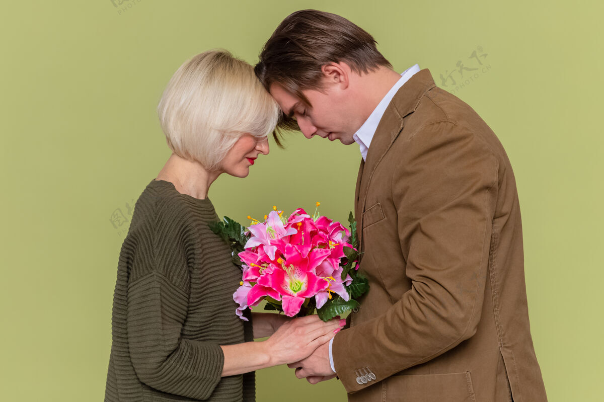 举办年轻美丽的情侣 热恋中的男女手持花束站在绿色的墙上庆祝国际妇女节花花束女人
