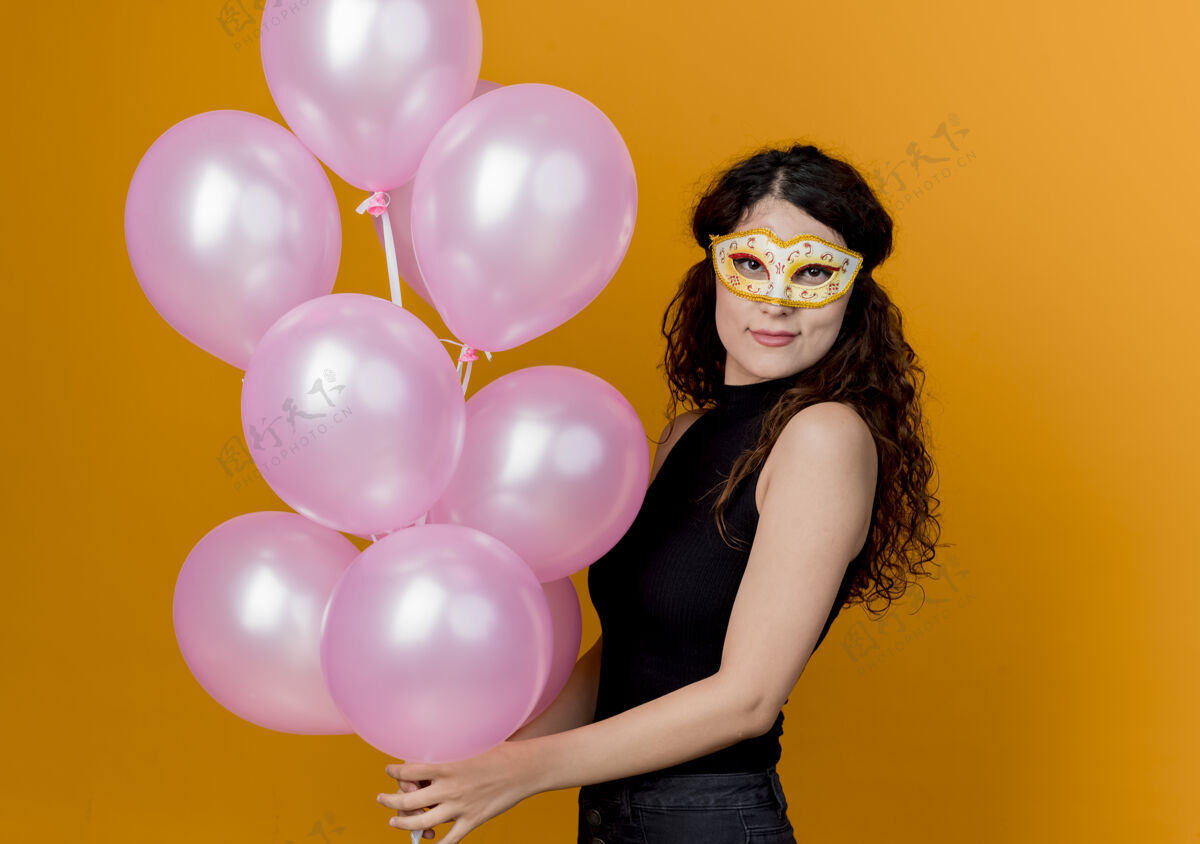 年轻年轻漂亮的女人卷发手持一束气球在派对面具快乐快乐的生日派对概念超过橙色美丽面具欢呼
