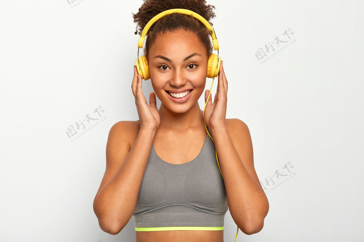 休息年轻女子喜欢音乐作为个人动力 双手戴着耳机 微笑愉快 穿着灰色运动内衣非洲快乐锻炼