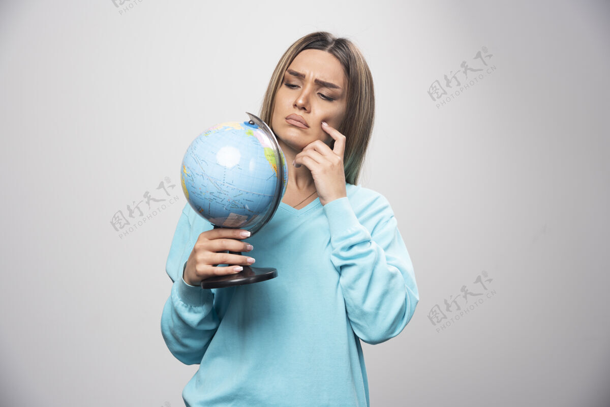 工人穿着蓝色运动衫的金发女孩手里拿着一个地球仪 仔细地思考 试图记住成人目的地女性