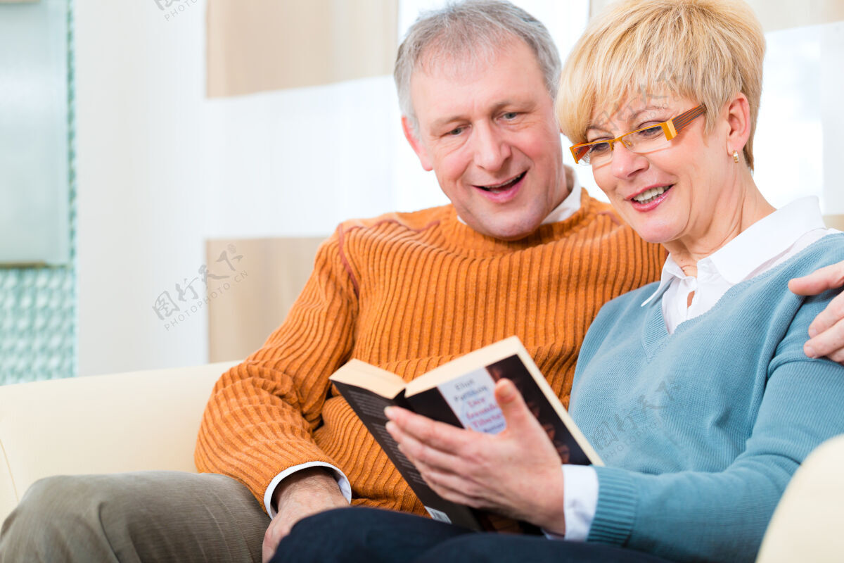 一起生活质量——两位老人坐在家里的沙发上 他拥抱着妻子拥抱阅读妻子