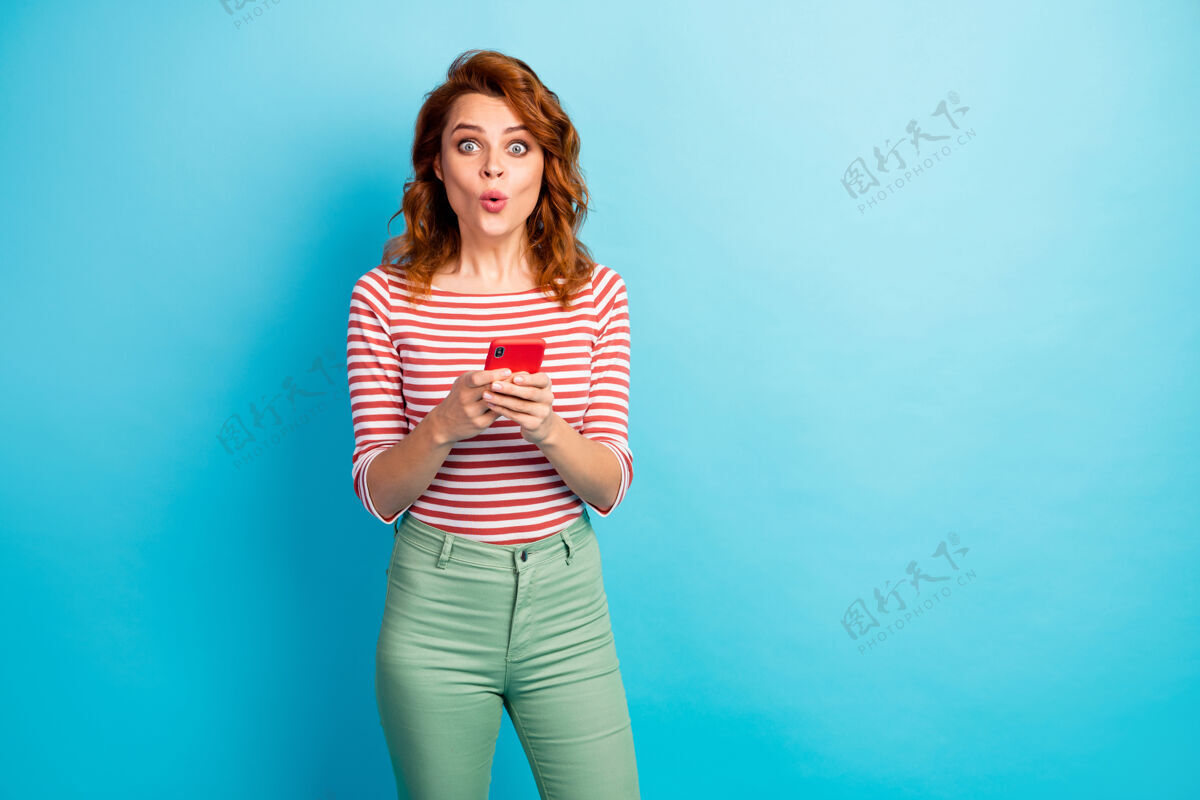 女性惊讶女孩的画像用手机阅读社交网络信息印象深刻尖叫哇哦omg穿好看的衣服隔离过蓝色裤子短信媒体