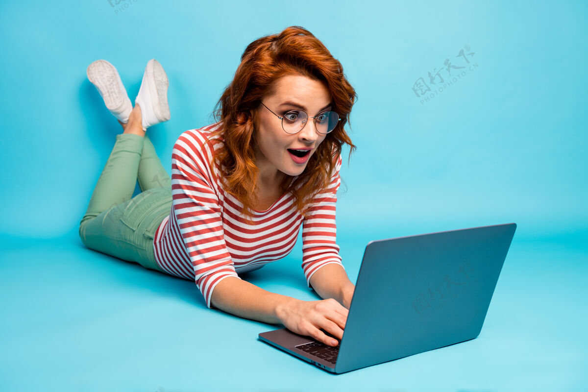阅读全尺寸特写照片疯女人躺在地板上工作笔记本电脑获得令人难以置信的博客通知印象深刻尖叫哇omg穿好看的运动鞋孤立的蓝色休闲同事年轻人