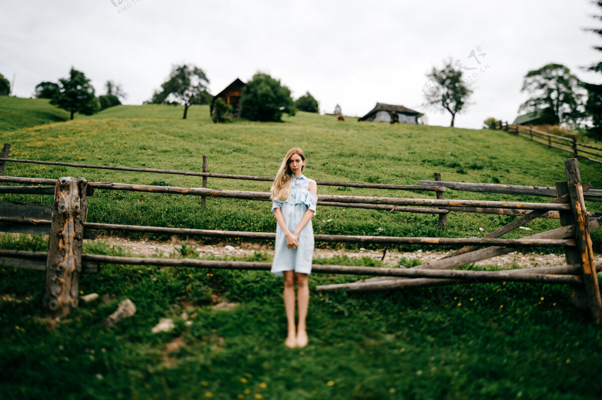 木头年轻漂亮的金发碧眼的女孩 穿着蓝色的裙子 在乡村的篱笆边摆姿势女人优雅姿势