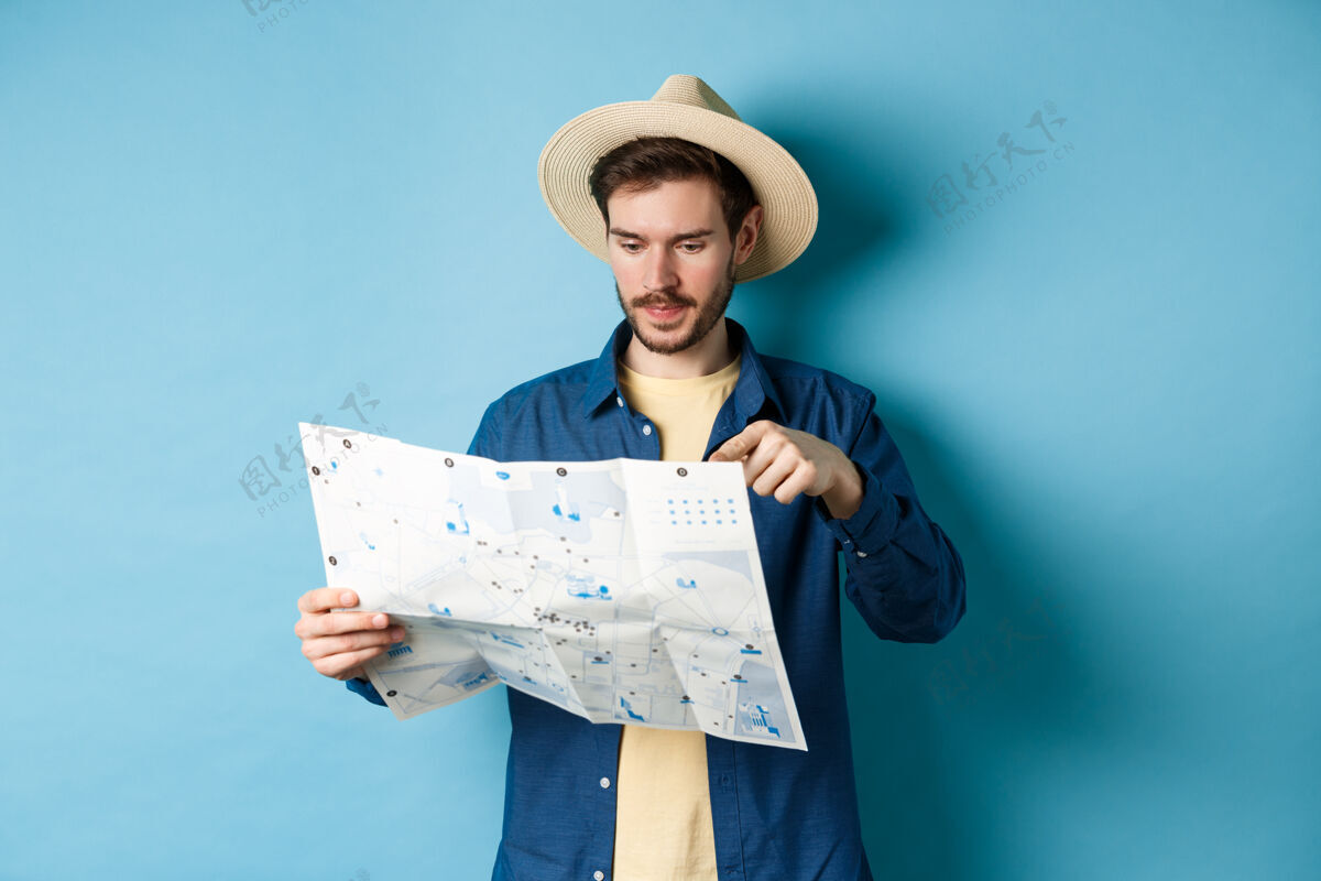 帽子帅哥选择去的地方 度假的时候指着地图 暑假的时候旅游 戴着草帽和衬衫 蓝色的背景站帅气休闲
