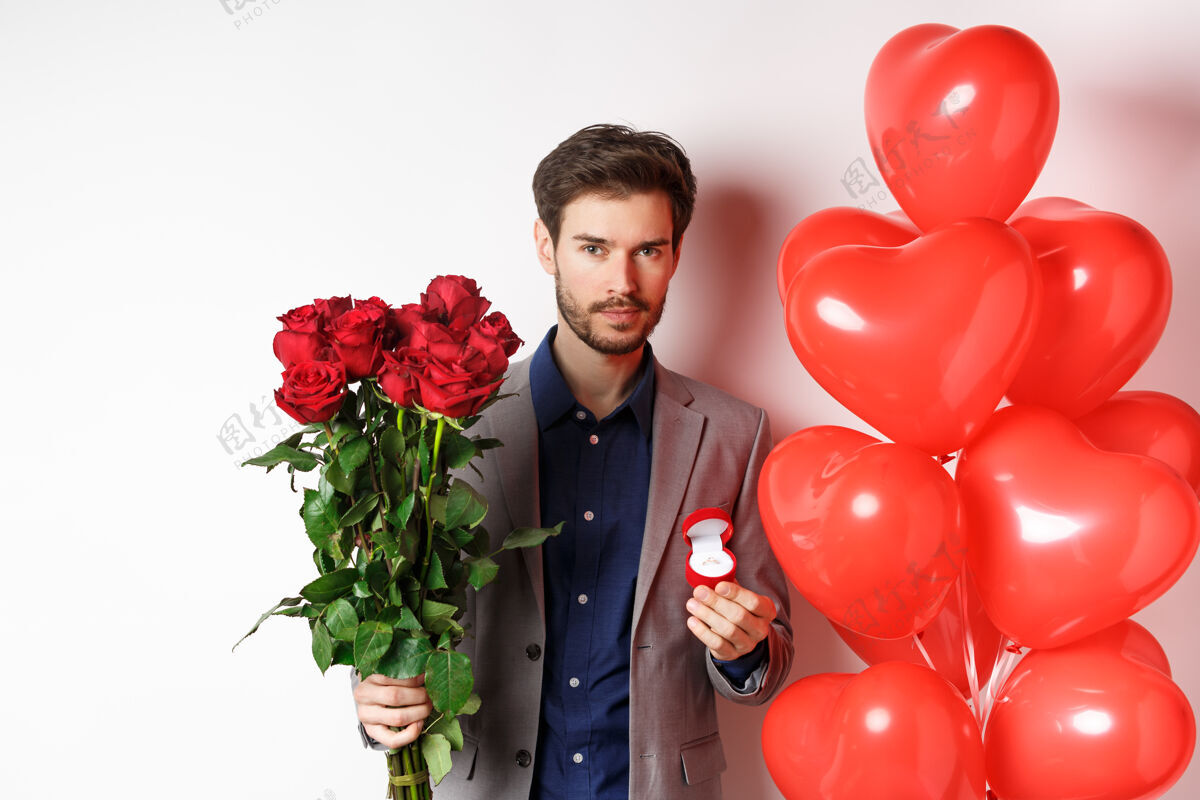 戒指帅哥准备求婚 捧着一束红玫瑰的订婚戒指 在情人节制造惊喜 站在心形气球旁 白色背景求婚心日子