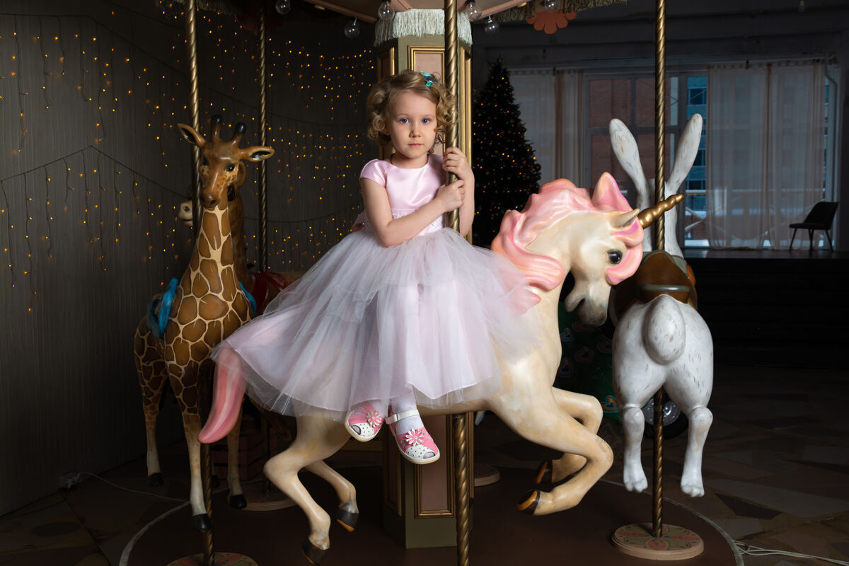 快乐一个穿着粉色裙子 戴着皇冠的女孩和一匹白色小马坐在旋转木马上公主旋转木马女孩