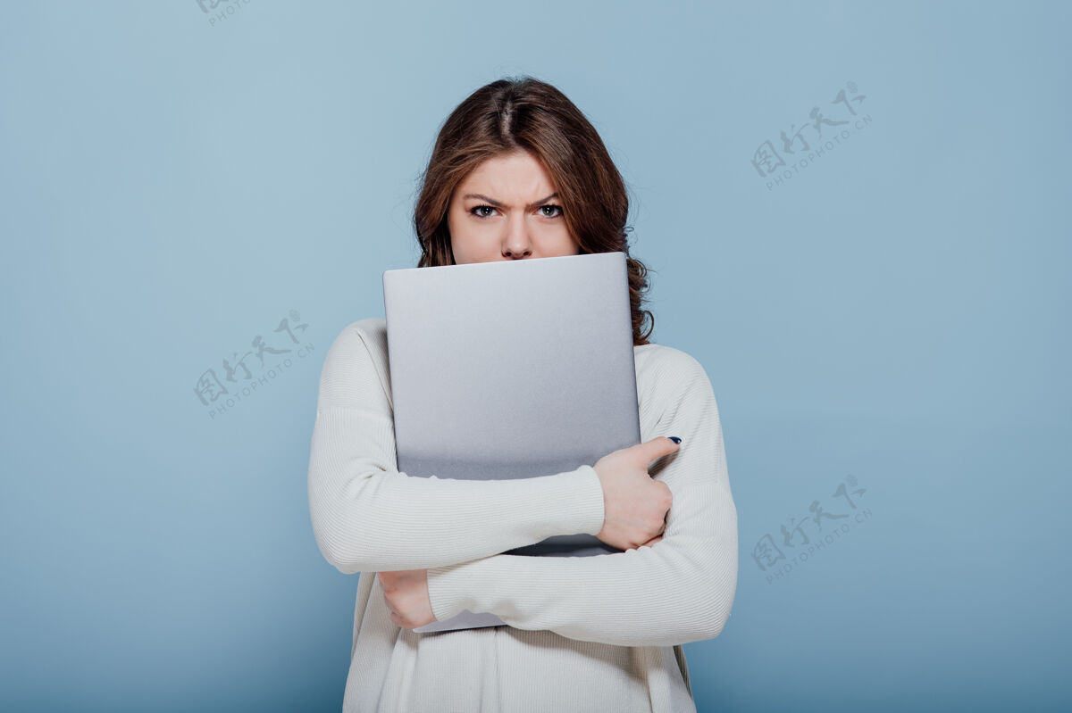 时尚不高兴的时尚女性皱眉 而拥抱笔记本电脑隔离在蓝色的墙壁青少年问题沮丧