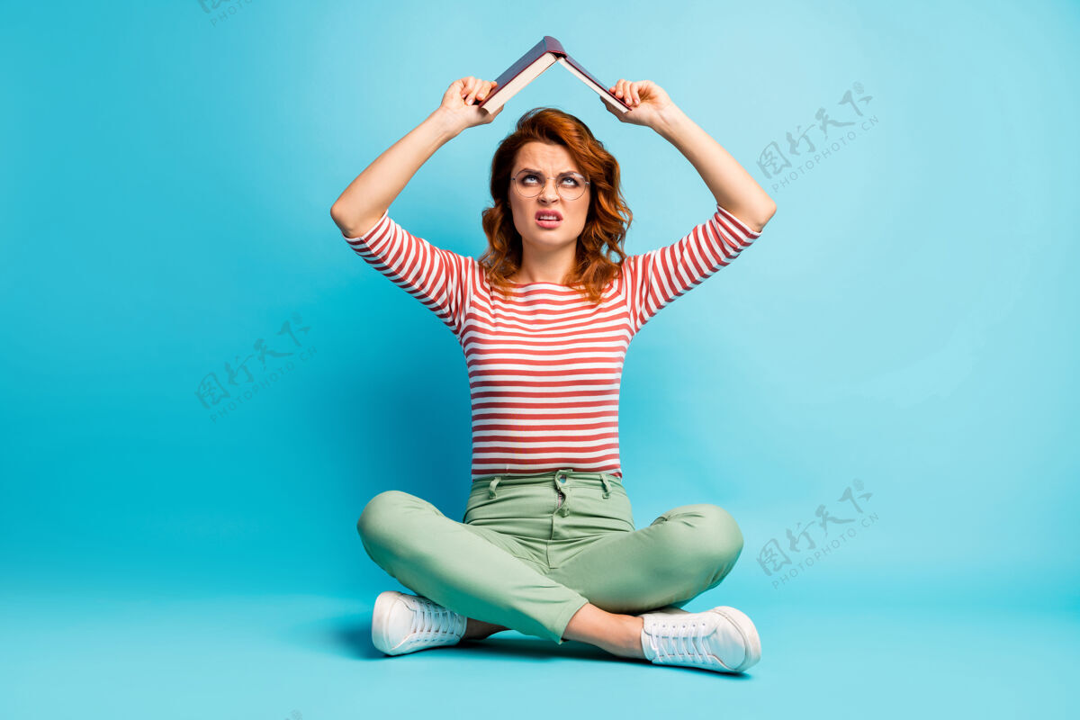 阅读Omg考试准备再次全身照片心烦意乱的女人坐着双腿交叉看头顶拿着纸质书不喜欢她的百科全书穿绿色时尚装孤立的蓝色裤子休闲信息