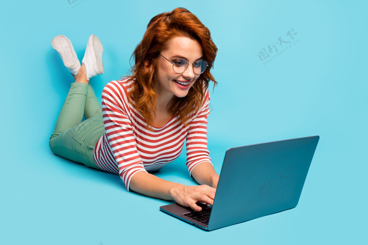 女人全身特写照片正面女人躺在地板上工作笔记本电脑有在线对话交流朋友同事穿白色胶鞋套头衫隔离蓝色条纹工人聊天