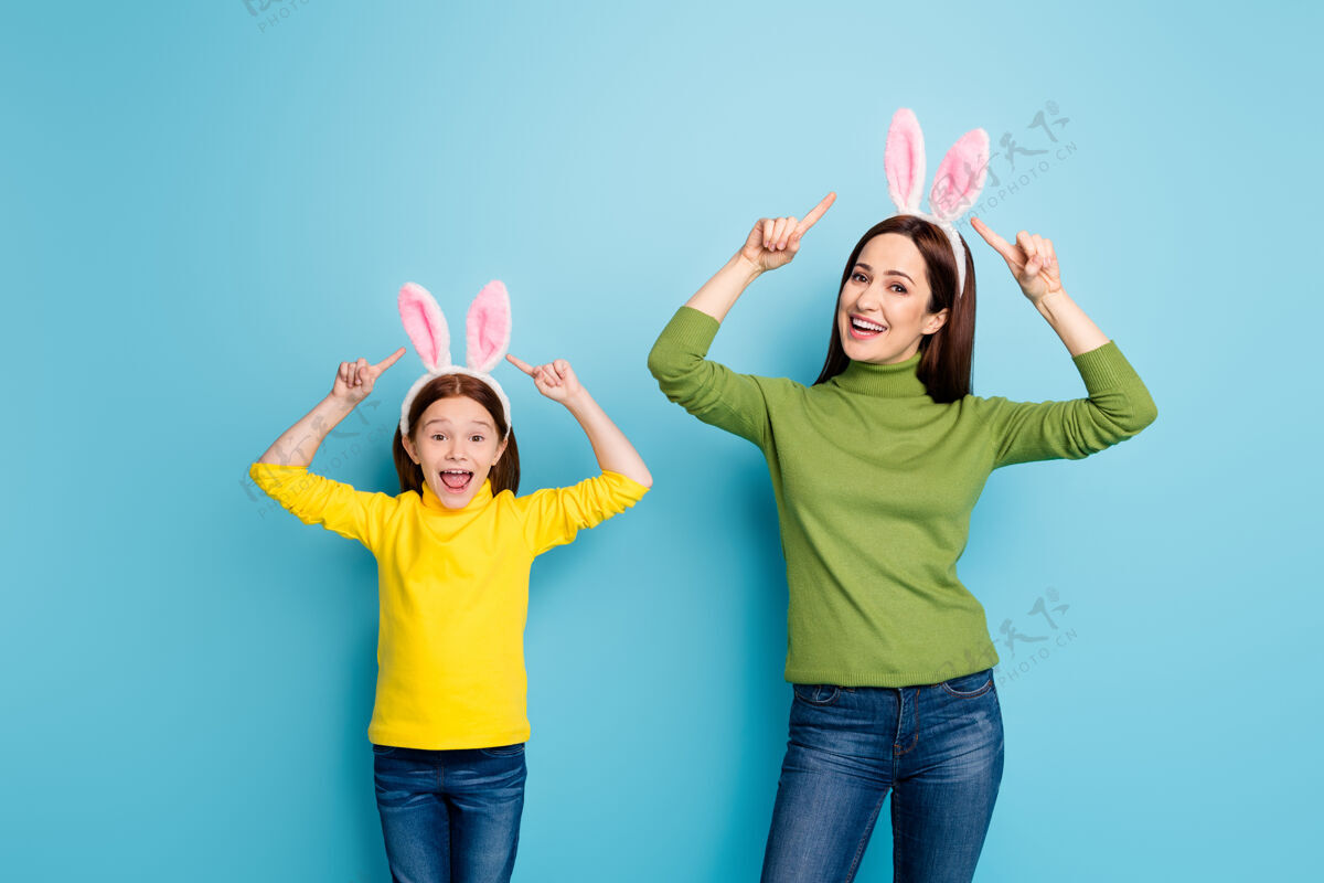 妈妈美丽迷人的肖像美丽开朗活泼的女孩戴着示范兔耳朵玩得开心孤立在明亮明亮明亮的光泽鲜艳的蓝色微笑童年兔子