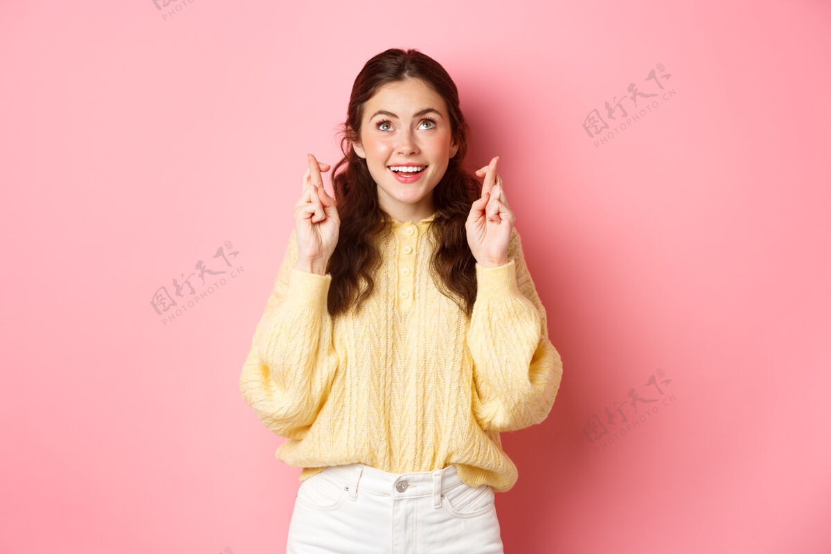 年轻可爱的女生祝通过考试 十指祝好运 抬头祈祷 微笑乐观 站在粉红色的墙上黑发咧嘴笑魅力
