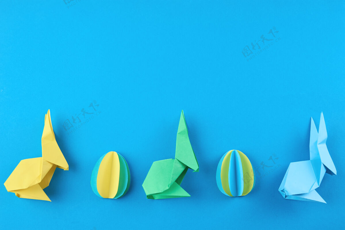 传统蓝色墙上的纸折纸兔子和彩蛋 俯视图复活节庆祝概念文化工艺节日