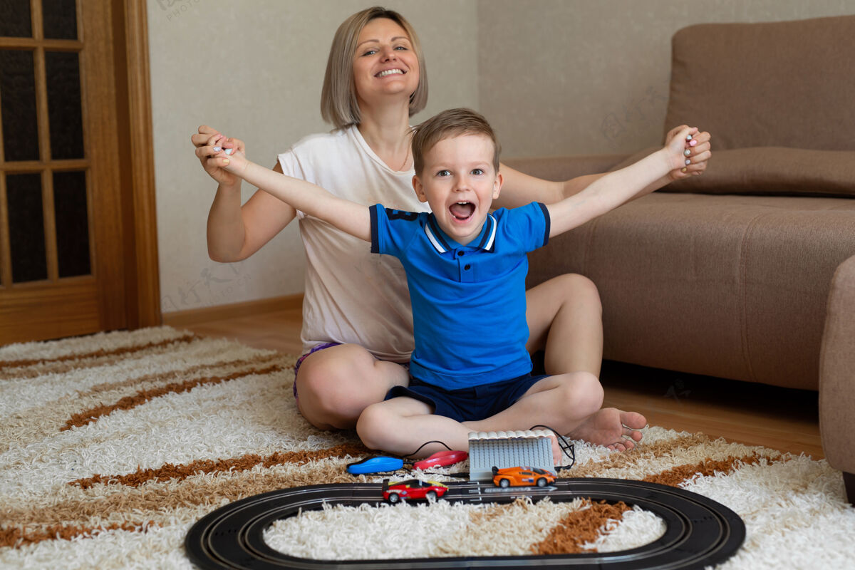 男孩妈妈和小儿子在家里的地毯上玩赛车 玩得开心又搂抱婴儿房间玩具