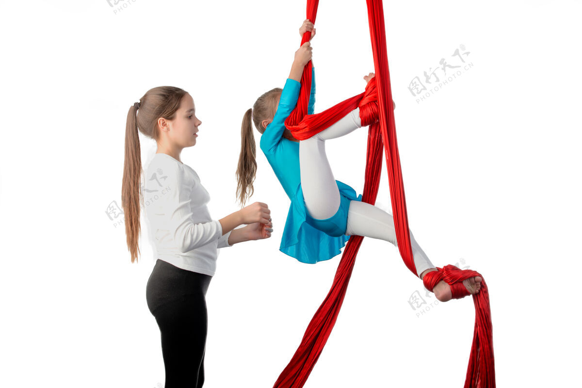 帮助十几岁的女孩帮助她的妹妹在杂技练习中正确地把自己固定在红色的空气丝带上健美操练习平衡