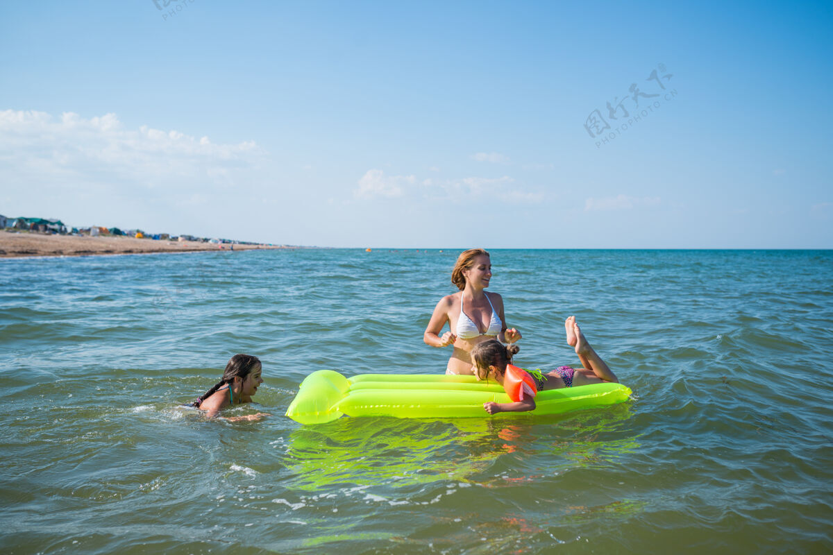 海岸一位积极的年轻家庭母亲和两个小女儿在黄色气垫上游泳的后视图空气海洋三天