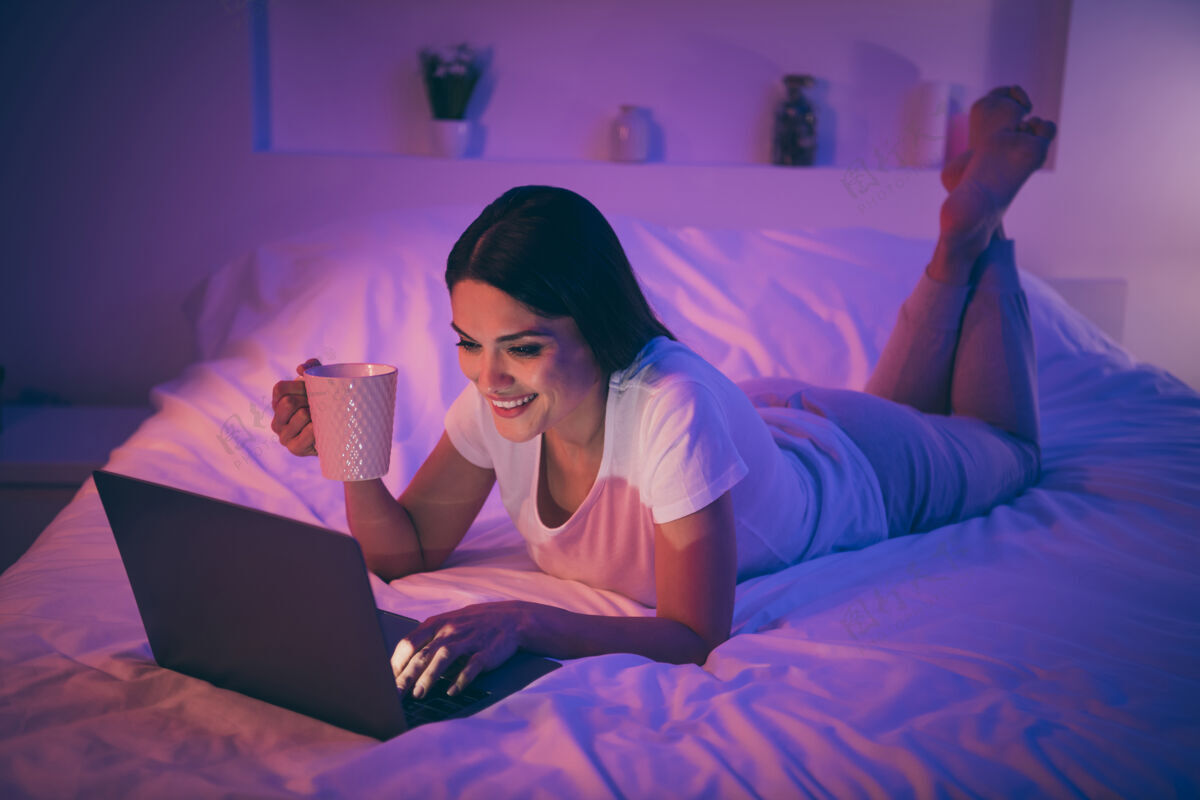 女人漂亮可爱开朗的女人躺在床上用笔记本电脑午睡睡衣快乐