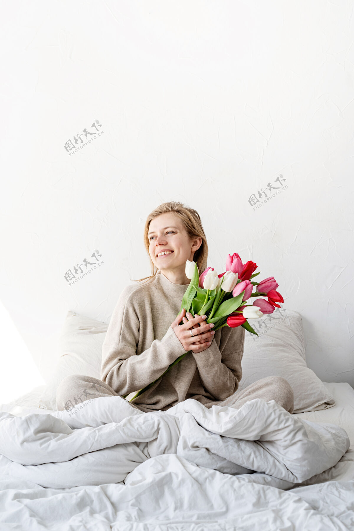 花快乐的女人穿着睡衣坐在床上 愉快地赏花女性室内礼物