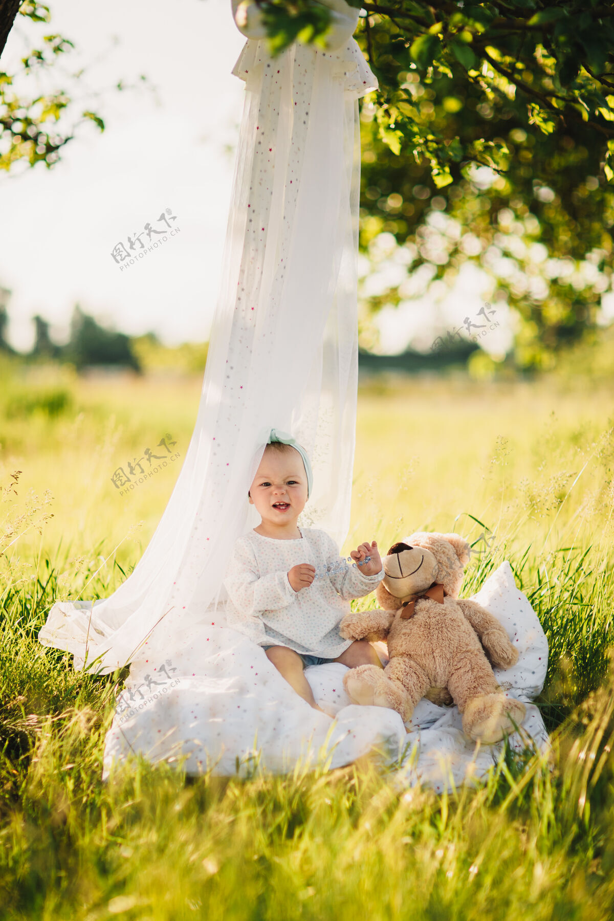 季节带着泰迪熊的小女孩坐在夏日阳光公园的白色毯子上自然美丽童年