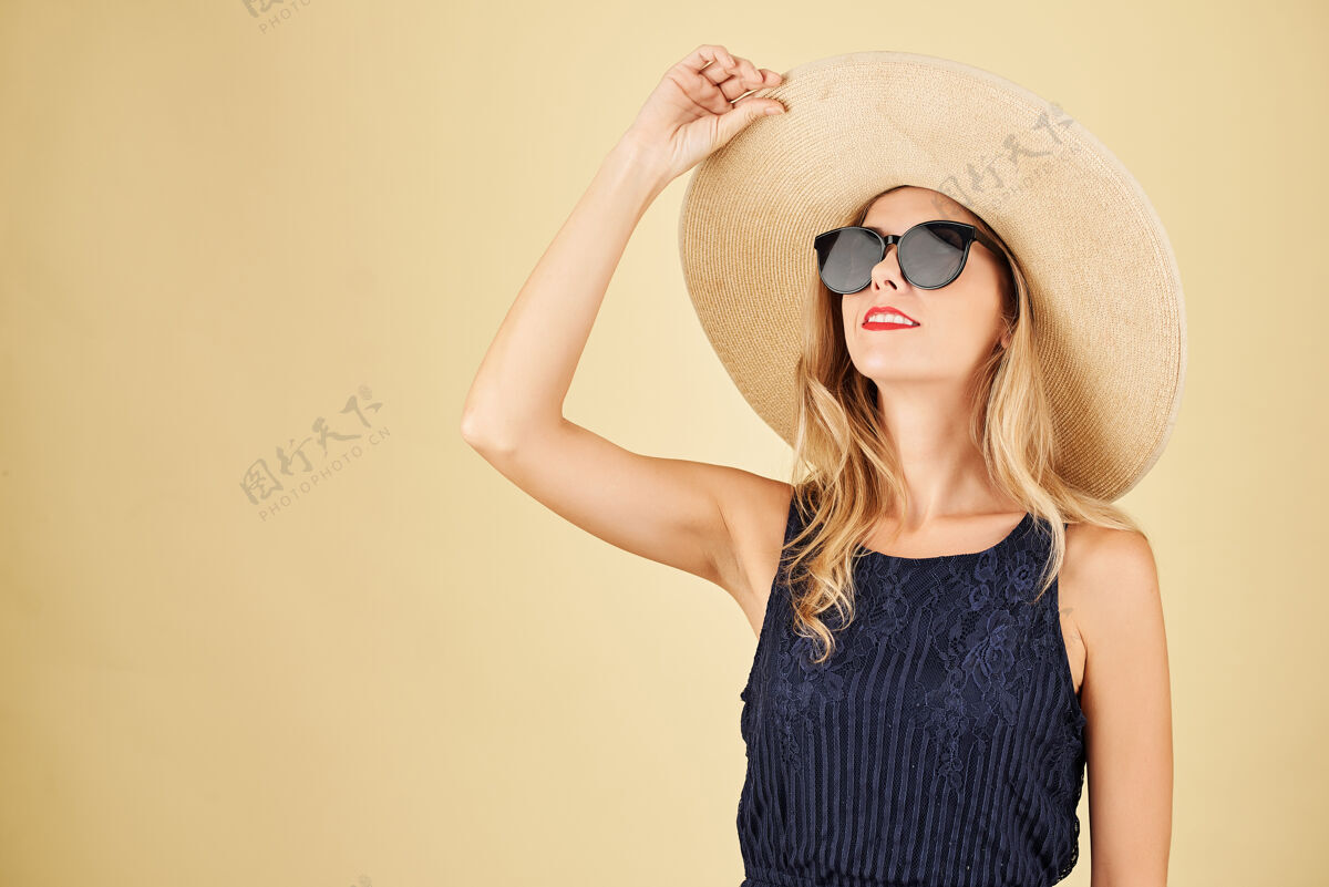 魅力戴着草帽和太阳镜的时髦年轻女子仰望的画像优雅金发欢呼