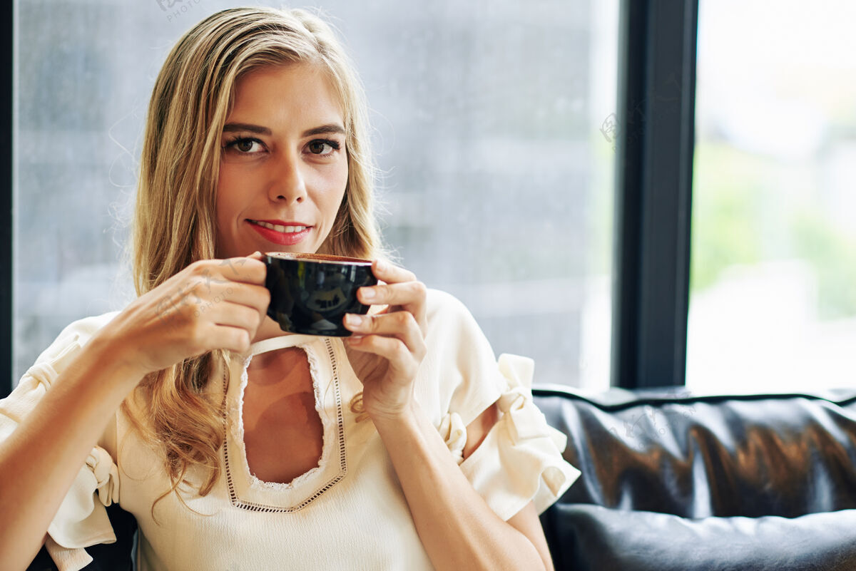 喝酒微笑迷人的年轻女子享受一杯热黑咖啡的画像坐着橱窗迷人的女性