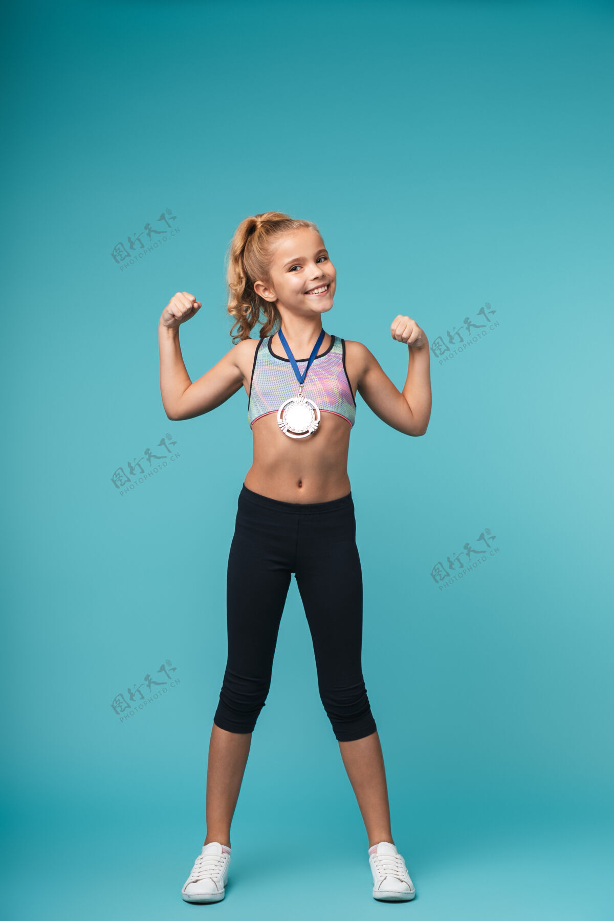 优胜者快乐的小运动女孩 戴着金牌 庆祝战胜蓝墙奖品荣誉地点