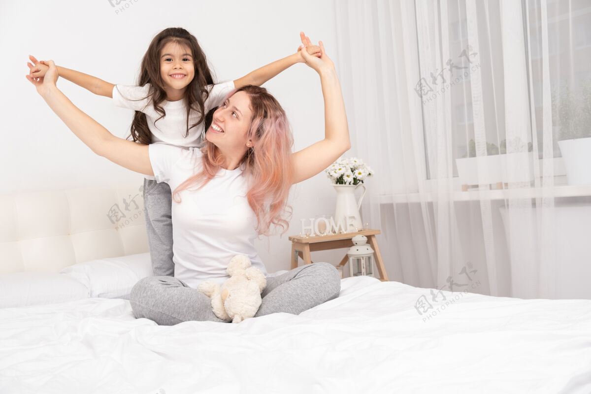 爱妈妈带着活泼的小女儿在家里的床上玩耍 玩得开心 和孩子们一起活动妈妈时间关心信任关系