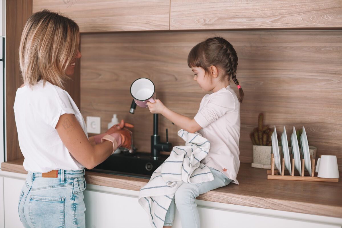 餐具小女孩在厨房里帮妈妈洗碗厨房女人她正在洗碗 女儿正在用毛巾擦杯子聚会生活方式厨房