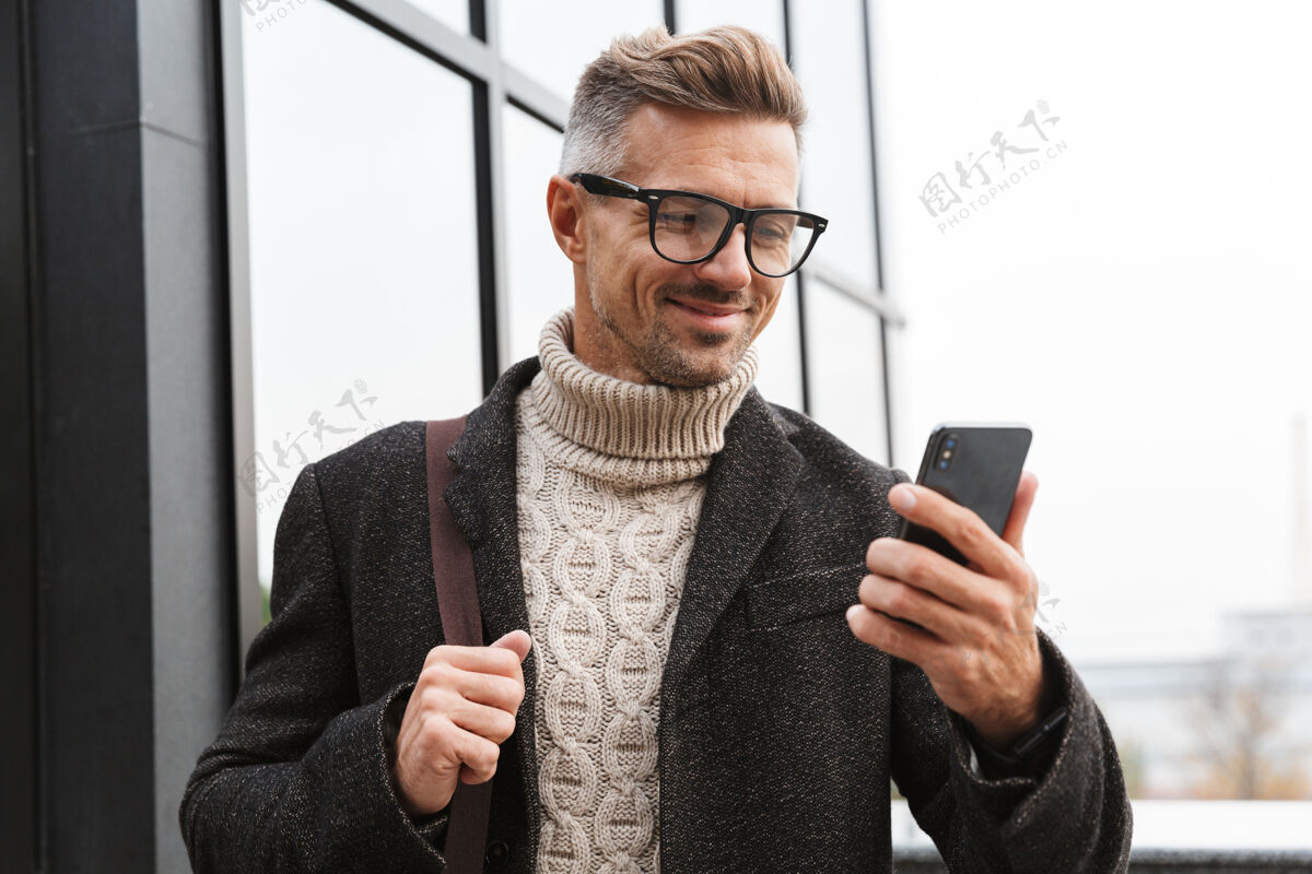 市中心30多岁的快乐男人戴着眼镜 穿过城市街道 使用智能手机聊天帅气电话