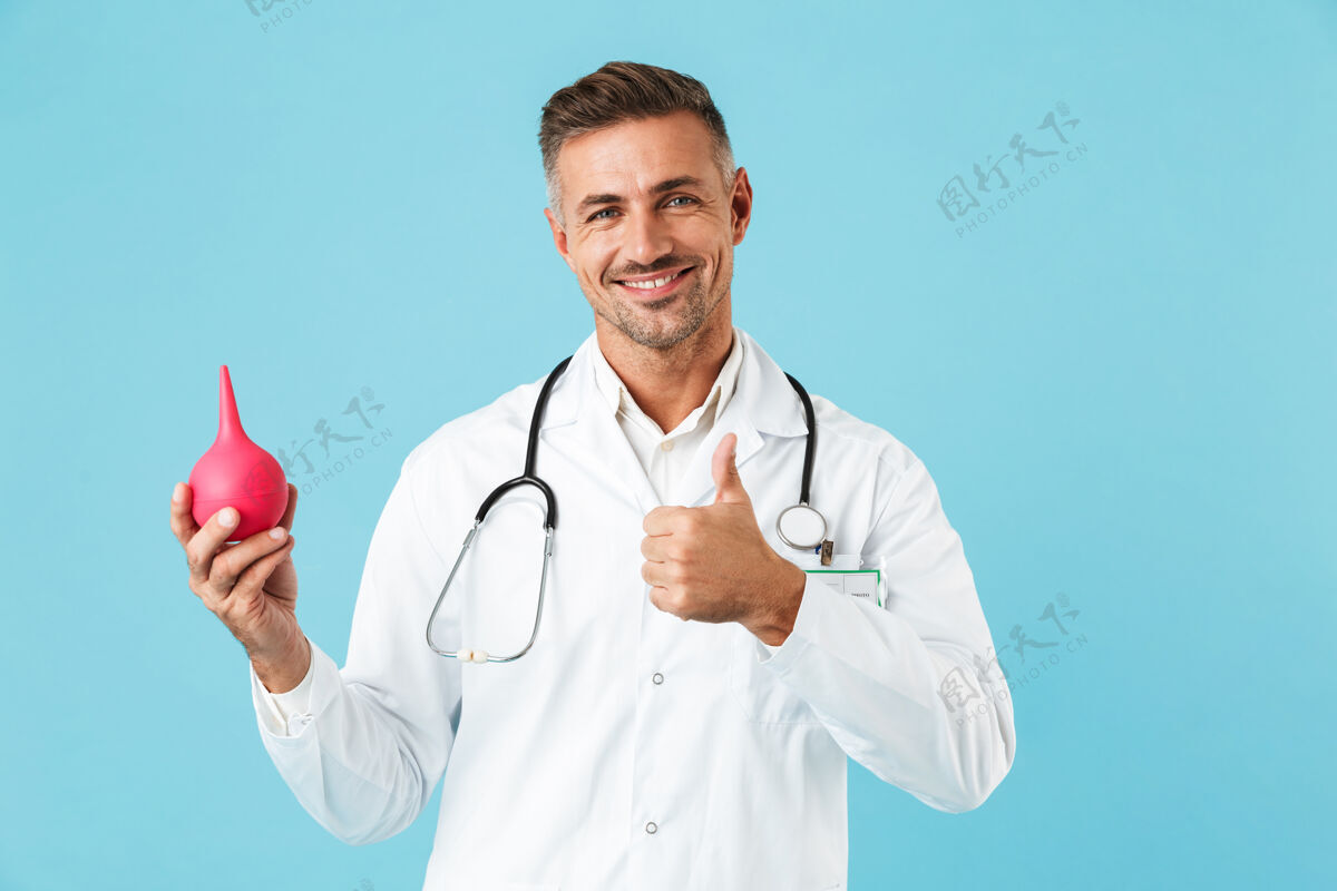 成熟快乐的医学专家穿着白大褂拿着灌肠器 孤立地站在蓝色的墙上医院成人工人