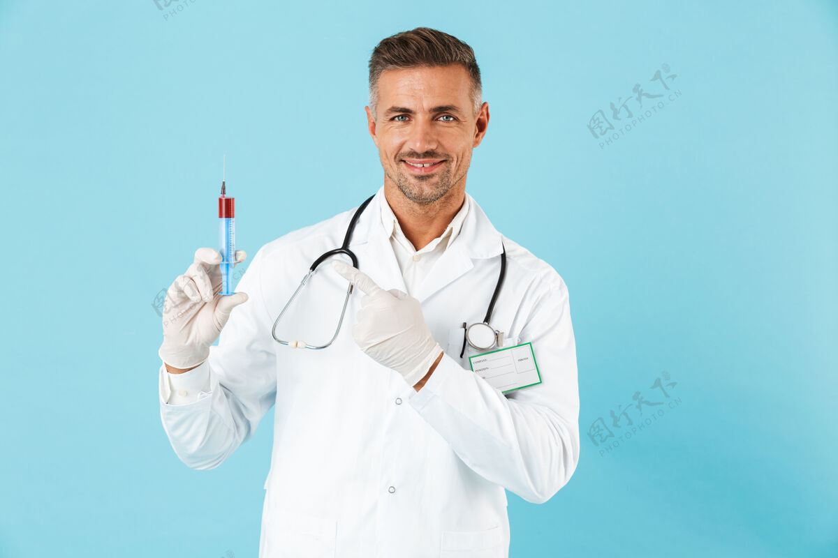 注射自信的男医生穿着制服 孤立地站在蓝色的墙上 展示着一个装有红色液体的注射器职业医生白种人