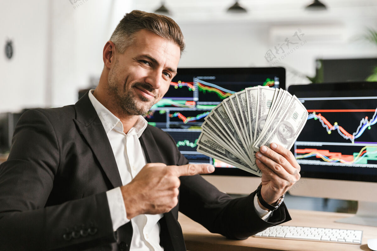 数据有吸引力的30多岁的商人穿着西装拿着钱扇在办公室工作 电脑上有图形和图表数字工作场所商业