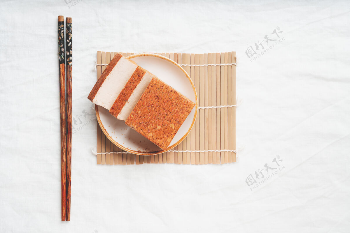 美味一块有机熟透的豆腐奶酪 放在白色盘子里 放在竹席上平铺顶视图素食小吃概念食物豆腐菜配料