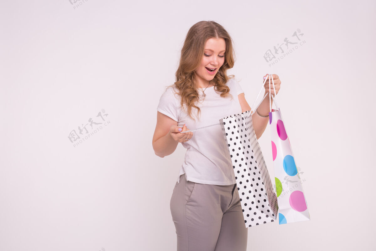 顾客快乐的欧洲金发女孩与彩色购物袋白色表面与复制空间消费者展台动作