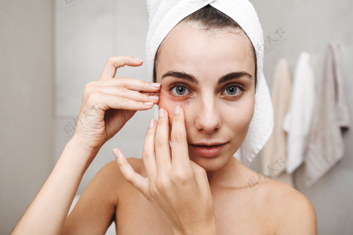 白种人特写镜头：一个头上戴着毛巾的漂亮年轻女子站在浴室里 敷眼罩皮肤护理毛巾吸引力