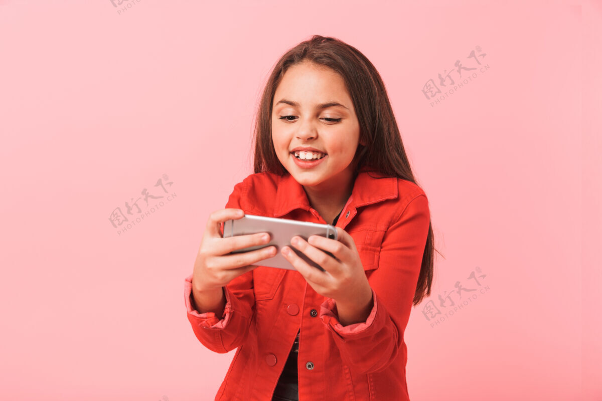 玩兴奋的少女在手机上玩视频游戏 而站着 隔着红墙孤立的形象电话女人爱