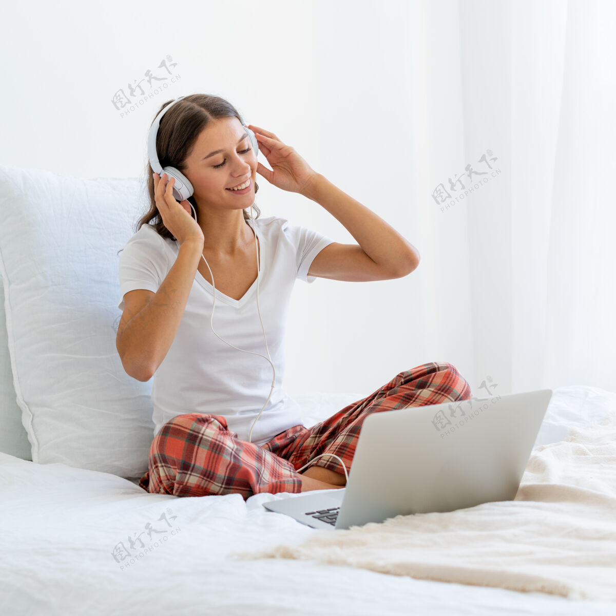 孤独坐在卧室的床上听音乐或看电影的微笑的年轻女人休闲聆听微笑